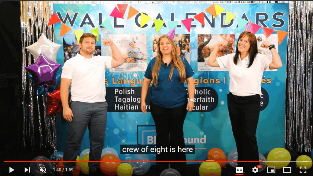 Photo of a video playing. WIth a picture of three people standing in front of a tradeshow booth that looks like it is having a party.